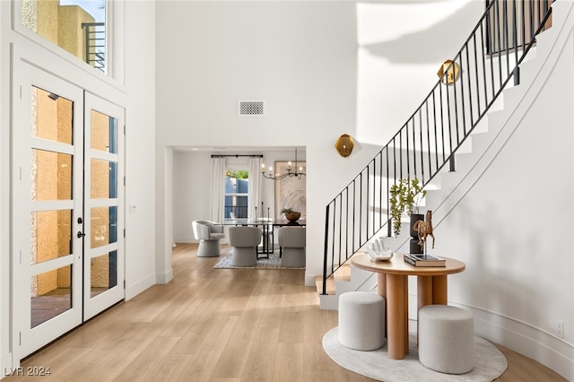 foyer featuring light hardwood / wood-style flooring, an inviting chandelier, french doors, and a towering ceiling