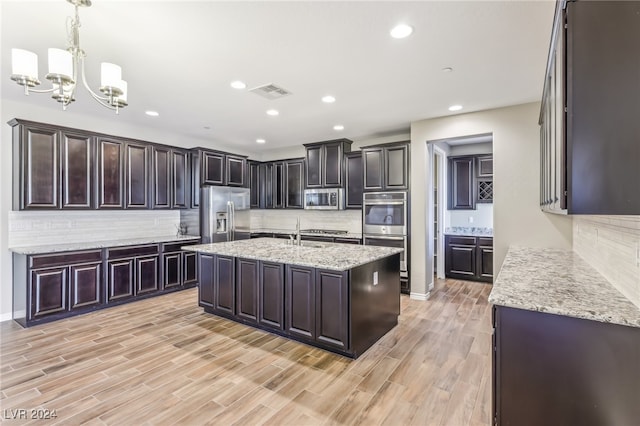 kitchen with stainless steel appliances, hanging light fixtures, a center island with sink, and light hardwood / wood-style flooring