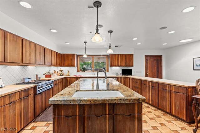 kitchen featuring sink, decorative light fixtures, an island with sink, and stainless steel gas stovetop