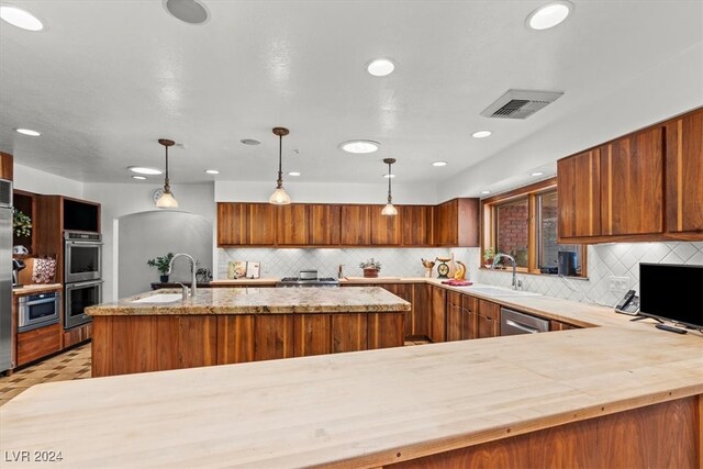 kitchen with kitchen peninsula, stainless steel appliances, hanging light fixtures, and sink