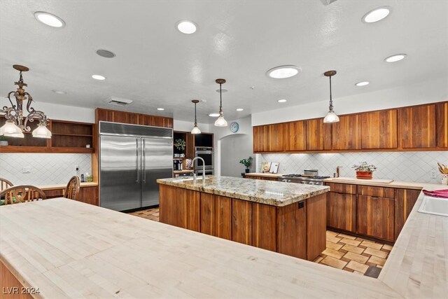 kitchen with a center island with sink, appliances with stainless steel finishes, tasteful backsplash, an inviting chandelier, and hanging light fixtures