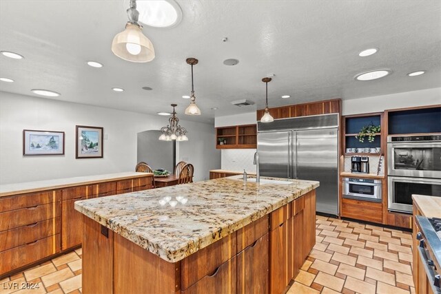 kitchen with a center island with sink, stainless steel appliances, light stone countertops, pendant lighting, and sink