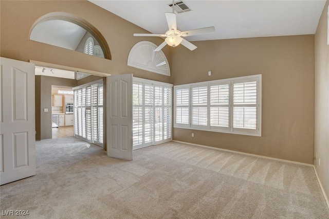 unfurnished room with light carpet, ceiling fan, and high vaulted ceiling