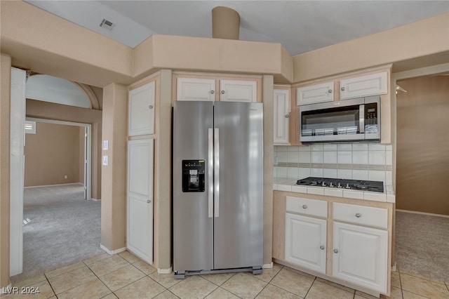 kitchen featuring light carpet, appliances with stainless steel finishes, decorative backsplash, white cabinetry, and tile counters