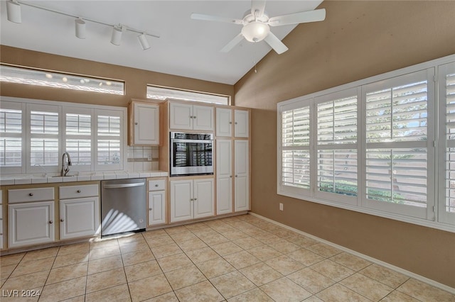 kitchen with a wealth of natural light, stainless steel appliances, vaulted ceiling, ceiling fan, and light tile patterned floors