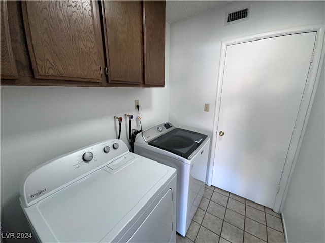 clothes washing area with cabinets, washer and clothes dryer, and light tile patterned floors