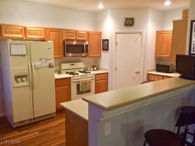 kitchen featuring kitchen peninsula, hardwood / wood-style flooring, and white appliances