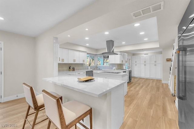 kitchen with island exhaust hood, visible vents, stainless steel dishwasher, white cabinets, and a peninsula