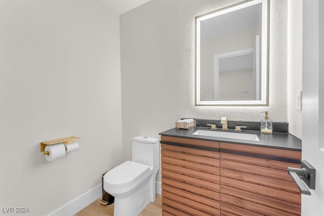 bathroom with toilet, a textured wall, baseboards, and vanity