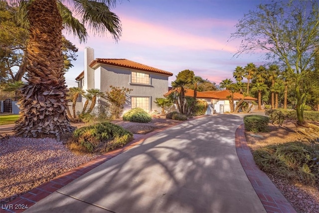 mediterranean / spanish house with a tiled roof, driveway, a chimney, and stucco siding