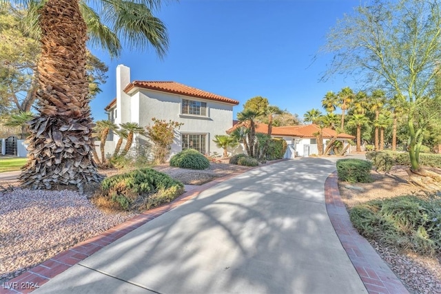 mediterranean / spanish-style home with a tile roof, driveway, a chimney, and stucco siding