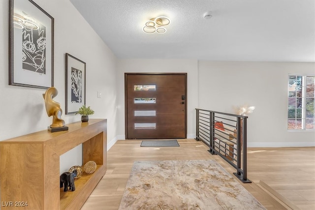 entrance foyer featuring light wood-style floors, a textured ceiling, and baseboards