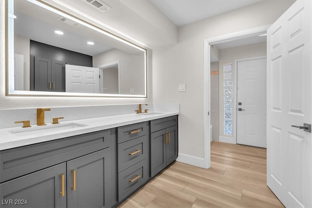 full bath with double vanity, visible vents, a sink, wood finished floors, and baseboards