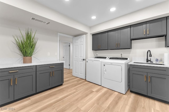 washroom with a sink, visible vents, light wood-style floors, independent washer and dryer, and cabinet space