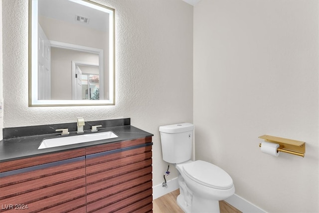 half bath with visible vents, a textured wall, toilet, wood finished floors, and vanity