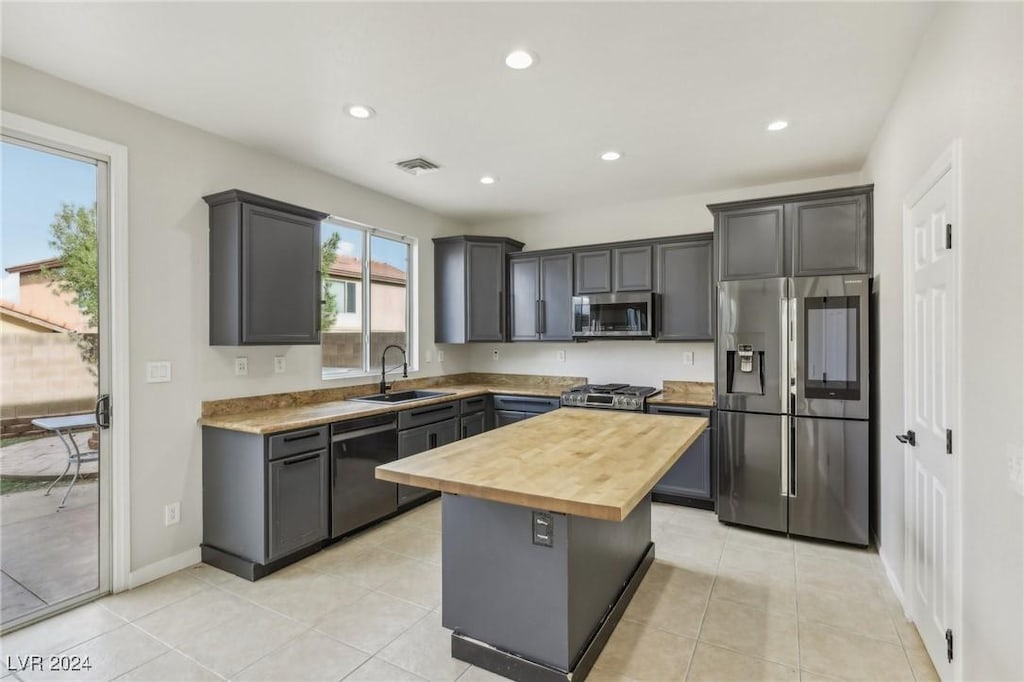 kitchen featuring gray cabinetry, sink, appliances with stainless steel finishes, butcher block countertops, and a kitchen island