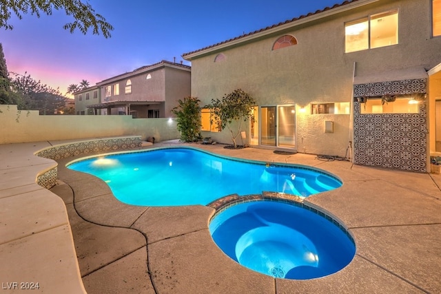 pool at dusk with an in ground hot tub and a patio area