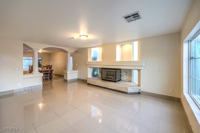 unfurnished living room with a fireplace, light tile patterned flooring, and decorative columns