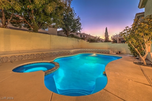 pool at dusk featuring a patio and an in ground hot tub