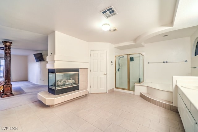 bathroom featuring tile patterned flooring, a tiled fireplace, vanity, and plus walk in shower