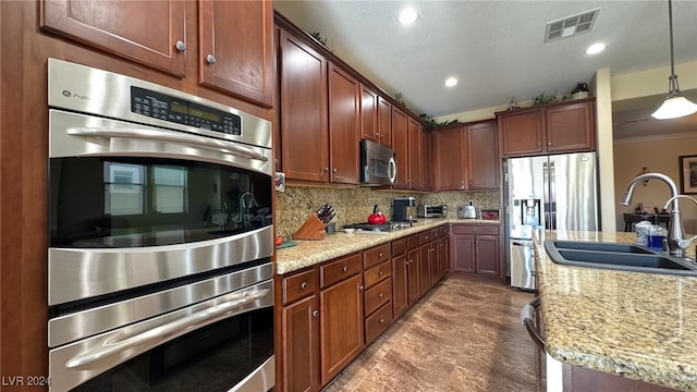 kitchen featuring stainless steel appliances, sink, tasteful backsplash, light stone countertops, and decorative light fixtures