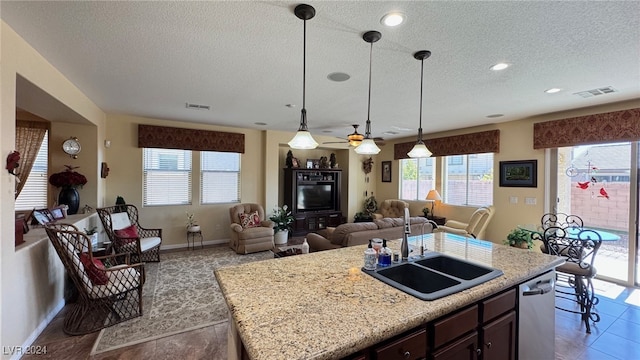 kitchen with a center island with sink, sink, a textured ceiling, decorative light fixtures, and stainless steel dishwasher