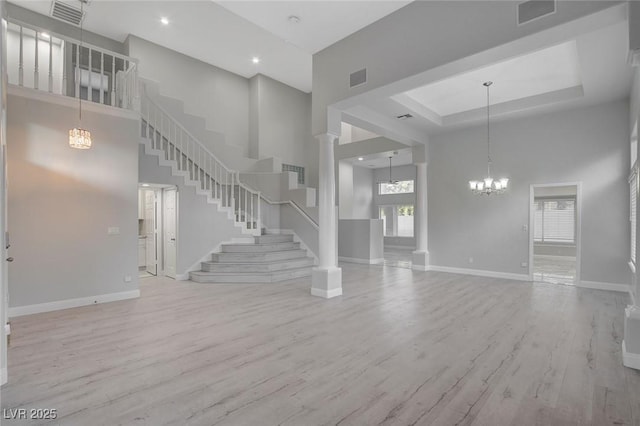 unfurnished living room with a towering ceiling, a raised ceiling, light wood-type flooring, and a notable chandelier