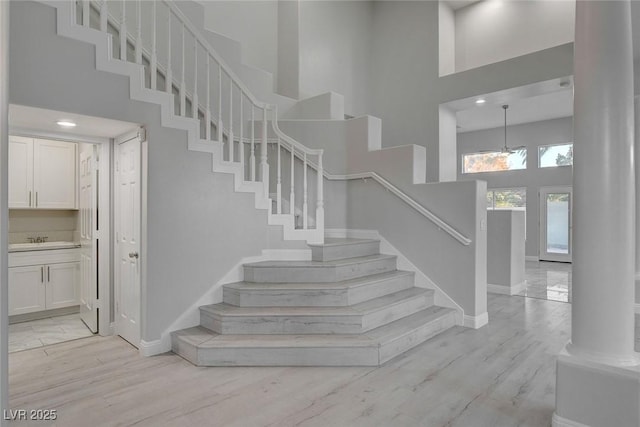 stairs with a high ceiling, sink, hardwood / wood-style floors, and decorative columns