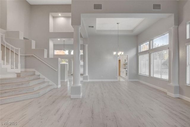 entryway with ornate columns, a tray ceiling, a notable chandelier, a towering ceiling, and light hardwood / wood-style floors