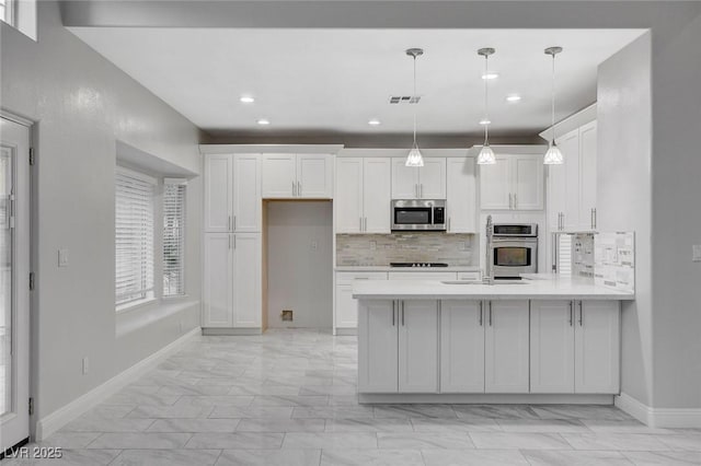 kitchen with tasteful backsplash, white cabinets, hanging light fixtures, kitchen peninsula, and stainless steel appliances