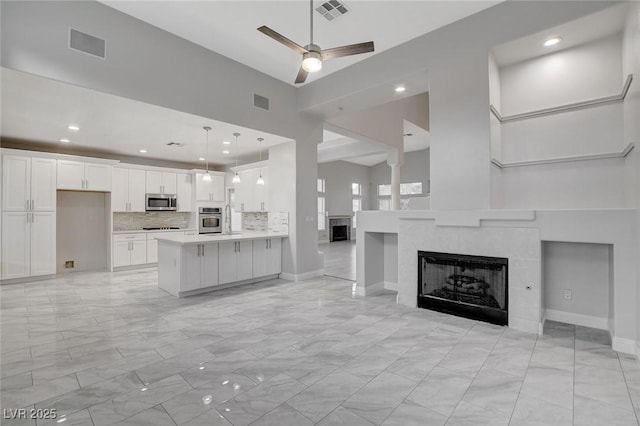 unfurnished living room with a tile fireplace, a towering ceiling, and ceiling fan