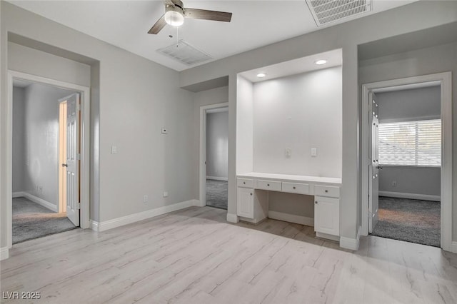 unfurnished bedroom featuring ceiling fan, built in desk, and light hardwood / wood-style floors