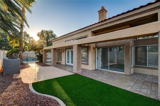 back house at dusk featuring a pool and a patio area