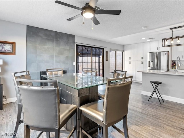 dining area featuring ceiling fan, sink, a textured ceiling, and light hardwood / wood-style floors