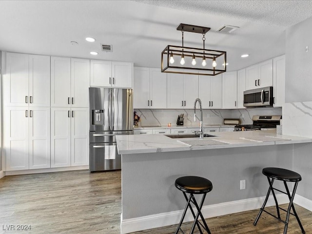 kitchen with decorative light fixtures, a kitchen bar, sink, stainless steel appliances, and white cabinets