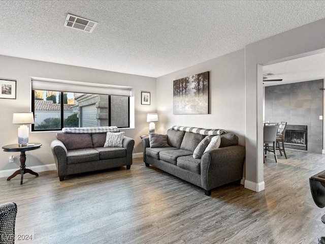 living room featuring a textured ceiling, ceiling fan, hardwood / wood-style flooring, and a tile fireplace