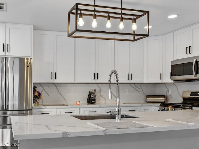 kitchen with tasteful backsplash, pendant lighting, sink, stainless steel appliances, and white cabinets