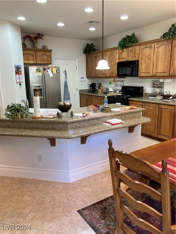 kitchen with a kitchen bar, black appliances, light tile patterned floors, and decorative light fixtures