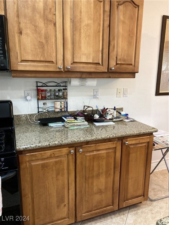 kitchen featuring black appliances, light tile patterned flooring, and stone countertops