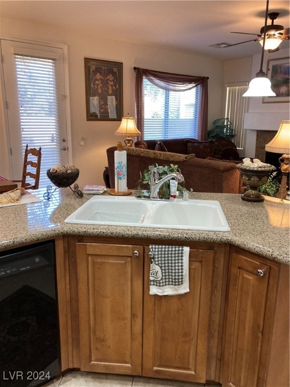 kitchen featuring black dishwasher, hanging light fixtures, sink, ceiling fan, and light stone countertops