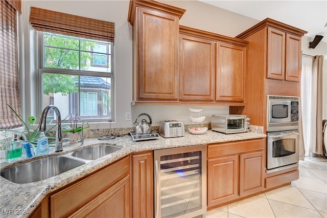 kitchen with light tile patterned flooring, wine cooler, sink, appliances with stainless steel finishes, and light stone counters