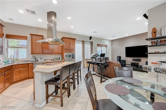 kitchen featuring a center island, stainless steel microwave, sink, a breakfast bar area, and island exhaust hood