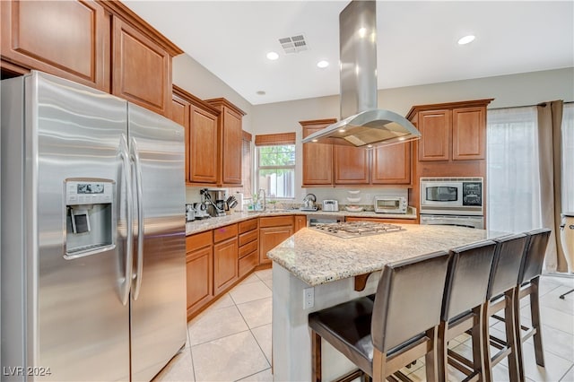 kitchen with island exhaust hood, appliances with stainless steel finishes, light stone countertops, a kitchen breakfast bar, and a center island