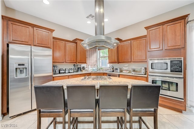 kitchen featuring stainless steel appliances, light tile patterned flooring, light stone countertops, a center island, and island exhaust hood