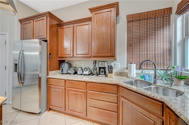 kitchen with light tile patterned flooring, light stone countertops, sink, and stainless steel fridge