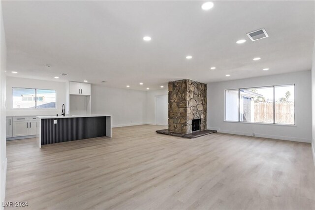 unfurnished living room with a stone fireplace, sink, and light wood-type flooring