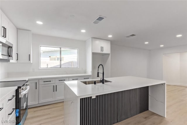 kitchen with white cabinetry, sink, appliances with stainless steel finishes, and an island with sink