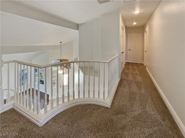 hall featuring dark colored carpet and an inviting chandelier