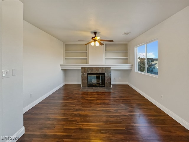 unfurnished living room with built in shelves, a tiled fireplace, dark hardwood / wood-style floors, and ceiling fan