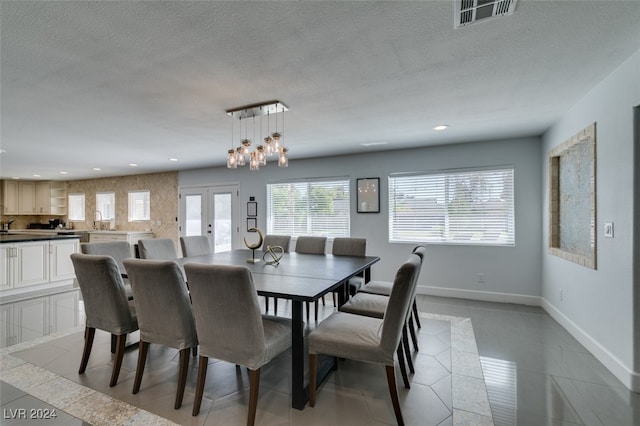 dining area with a textured ceiling, light tile patterned floors, an inviting chandelier, and french doors